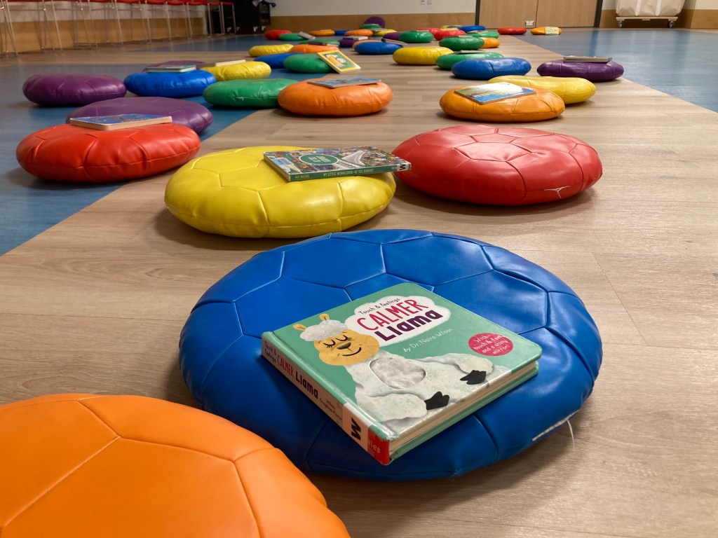 Board books laid out on brightly colored cushions in the programming room before Ingrid Christina's Ukulele Baby Lap Time program 